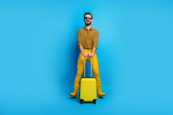 Full length photo excited bearded man hold carry his trolley luggage enjoy air check in tourism verification wear checkered clothes footwear bright pants look isolated blue color background — 스톡 사진