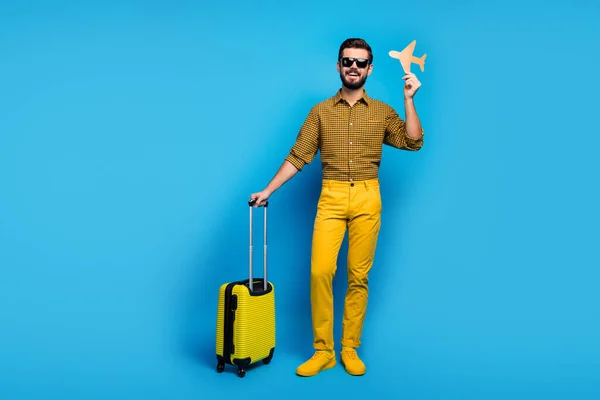 Full body photo positive bearded man enjoy tourism weekends hold orange papercard plane trolley travel air first-class wear checkered outfit bright pants gumshoes isolated blue color background — 스톡 사진