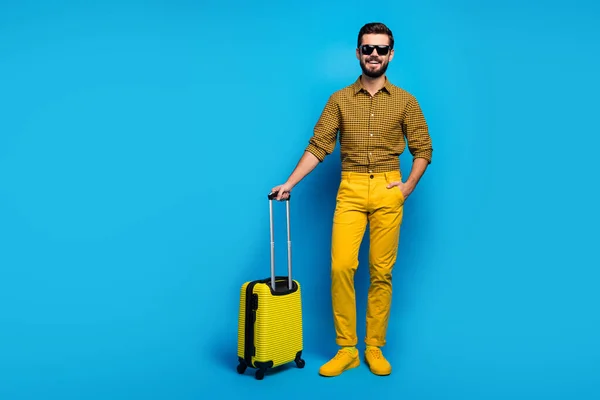 Full size photo positive bearded guy tourist enjoy air voyage stand in terminal wait check-in hold total yellow rest look trolley wear xadrez clothes sneakers isolated blue color background — Fotografia de Stock