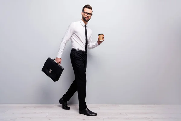 Perfil de longitud completa lado foto marketer economista hombre ir caminar mañana sociedad reunión celebrar bebida taza bolso de cuero desgaste camisa blanca pantalones negros aislados color gris fondo — Foto de Stock