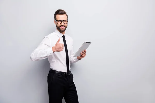 Portrait of confident cool positive leader man freelancer use tablet show thumb up sign approve partnership wear white black pants trousers isolated over grey color background