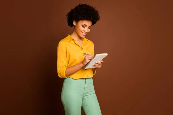 Photo of attractive dark skin curly lady author look diary noting creative thoughts writing comments inspired wear yellow shirt green trousers isolated brown color background — 스톡 사진