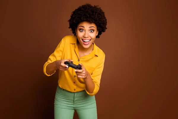 Photo of crazy funny dark skin wavy lady hold joystick plying video game addicted gamer online team leader wear yellow shirt green pants isolated brown color background — 스톡 사진