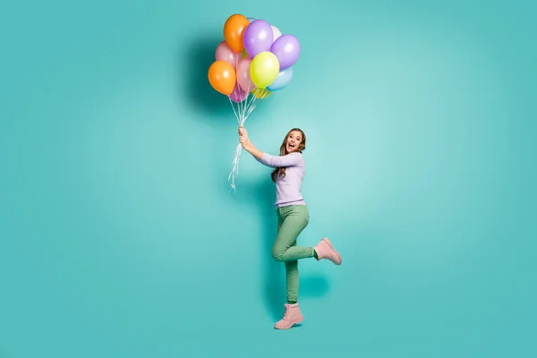 Full length profile photo of pretty funky lady hold many colorful air balloons gonna fly away with wind blowing wear lilac jumper green pants boots isolated teal pastel color background — 스톡 사진
