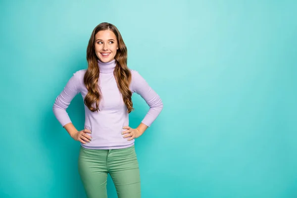 Photo of beautiful pretty lady long curly hairstyle good mood hands by sides look empty space wondered wear lilac purple sweater green trousers isolated pastel blue color background — 스톡 사진