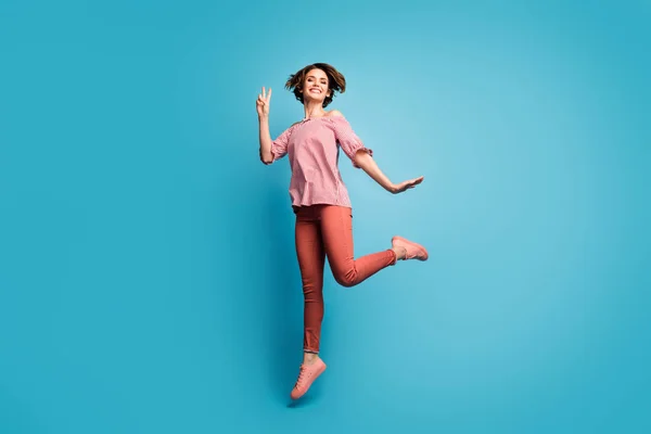 Full body profile photo of beautiful pretty lady jumping high good mood showing v-sign symbol wear casual white red open shoulders blouse pants isolated blue color background — 图库照片