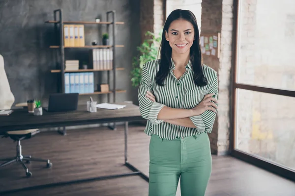 Photo of attractive cheerful latin business lady arms crossed reliable person meet partners friendly smiling assistant wear striped shirt green pants standing modern office indoors — 图库照片
