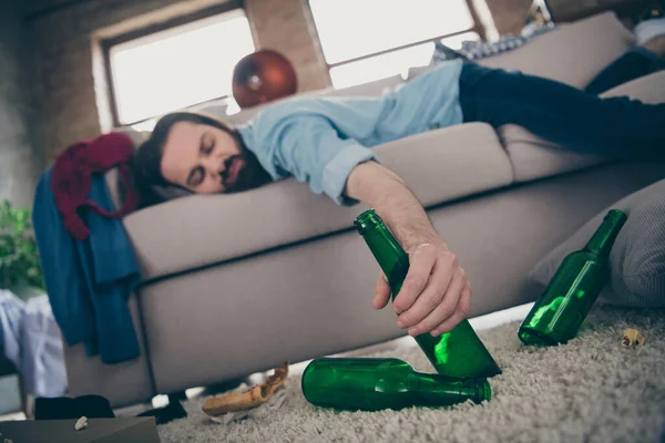 Photo of hopeless boozer guy lying sofa taking beer bottle pizza pieces on floor had crazy entertainment suffering after party hangover morning headache messy flat indoors — 图库照片