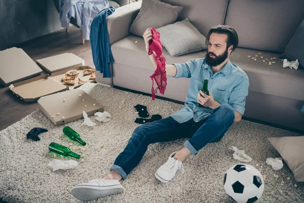 Above high angle view of his he nice attractive sick shocked confused bearded guy sitting on floor finding girls left things after party at home living-room house flat indoors