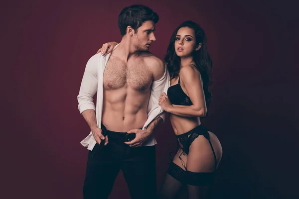 Photo of two hot people macho husband unfasten pants belt look at mistress bikini wife taking off his shirt enjoy submission role play game isolated maroon color background