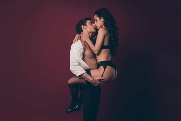 Profilul fotografie de tandrețe excitat doi oameni soțul ține mâinile șolduri ridica nud fierbinte negru bikini soție tentant sărutat corp viril brațe puternice izolate fundal de culoare burgundy — Fotografie, imagine de stoc