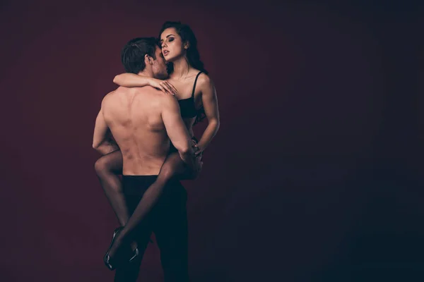 Rear view photo of two horny people handsome topless husband hold hands raise nude hot black boudoir wife smell kiss perfect body strong arms isolated maroon color background — Stockfoto