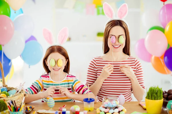 Close-up portrait of nice attractive funky creative cheerful girls small little pre-teen sister wearing bunny ears covering eyes with decorative eggs in white light interior room house — Stock Photo, Image