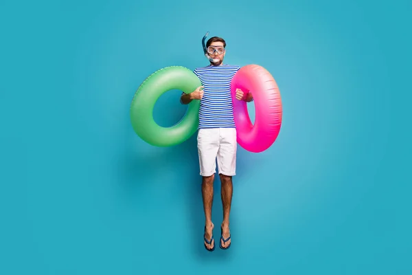 Full length photo of funky crazy guy tourist jump high swimming water mask tube two pink green lifebuoy wear striped sailor shirt shorts flip flops isolated blue color background — 스톡 사진