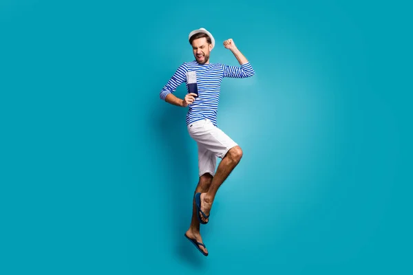 Full length profile photo of funky guy tourist jump high celebrating vacation start getting visa wear striped sailor shirt vest cap shorts flip flops isolated blue color background — Stockfoto