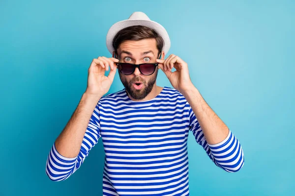 Photo of funky excited handsome guy tourist taking off cool black sun specs open mouth read discounts banner wear striped sailor shirt cap isolated blue color background — Stockfoto