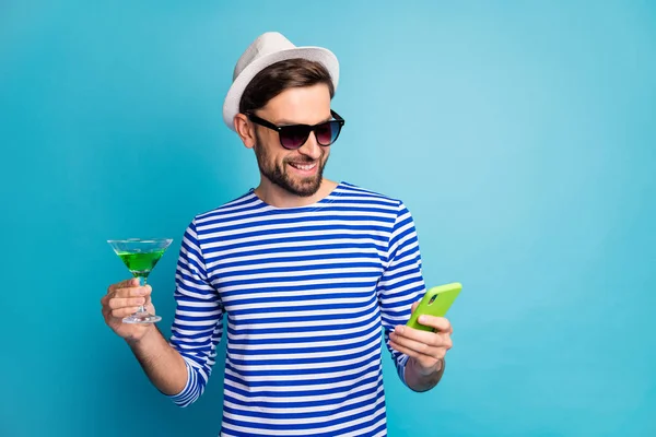 Photo of funky traveler guy browsing telephone drink green alcohol cocktail all inclusive exotic resort wear sun specs striped sailor shirt cap isolated blue color background — ストック写真