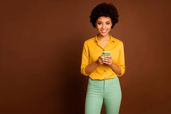 Photo of funny dark skin faliste lady trzymając telefon ręce influencer otwarte usta czytać pozytywne komentarze nosić żółtą koszulę zielone spodnie odizolowane brązowy kolor tła — Zdjęcie stockowe