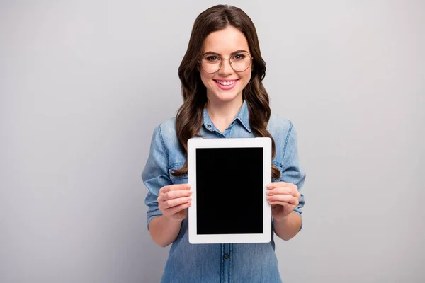 Photo of beautiful freelancer lady hold e-reader tablet demonstrating new gadget model sale low price wear specs casual jeans denim shirt isolated grey color background — Stock Photo, Image