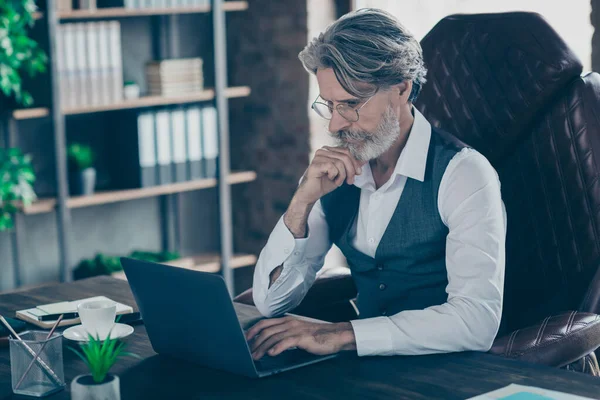 Nahaufnahme Porträt seines schönen attraktiven gutaussehenden, fokussierten, grauhaarigen Herrn, der im Stuhl sitzt und auf einem Laptop am Arbeitsplatz im Loft-Stil nach Daten sucht — Stockfoto