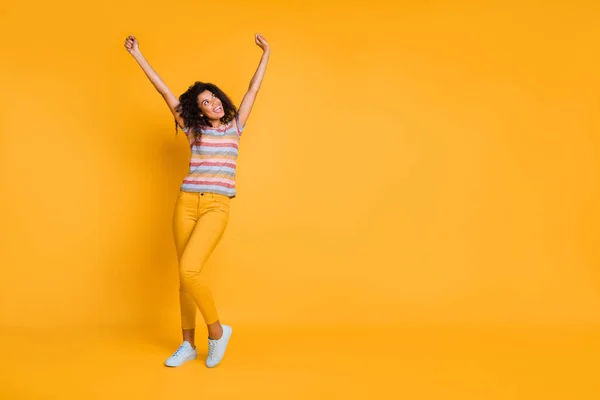 Comprimento total tamanho do corpo vista de agradável atraente alegre alegre menina de cabelos ondulados usando listrado t-shirt levantando as mãos para cima se divertindo isolado no brilhante brilho vívido vibrante cor amarela fundo — Fotografia de Stock