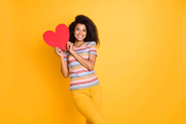 Retrato de bonita chica alegre alegre alegre de pelo ondulado en camiseta a rayas sosteniendo en las manos corazón centro de la clínica de salud humana aislado en brillante brillo vivo vibrante color amarillo fondo —  Fotos de Stock