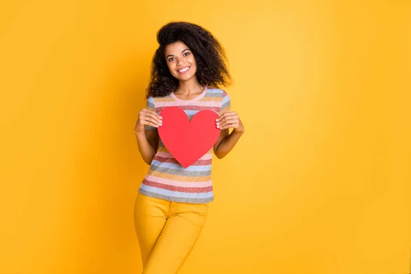 Retrato de agradable atractiva alegre alegre tipo ondulado de pelo chica de rayas camiseta sosteniendo en las manos corazón cuidado de la salud humana medicina aislada en brillante brillo vivo vibrante color amarillo fondo —  Fotos de Stock