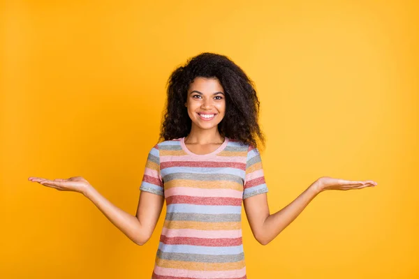 Portrait of her she nice attractive cheerful cheery wavy-haired girl wearing striped tshirt holding on palms two invisible objects isolated on bright vivid shine vibrant yellow color background — Stock Photo, Image