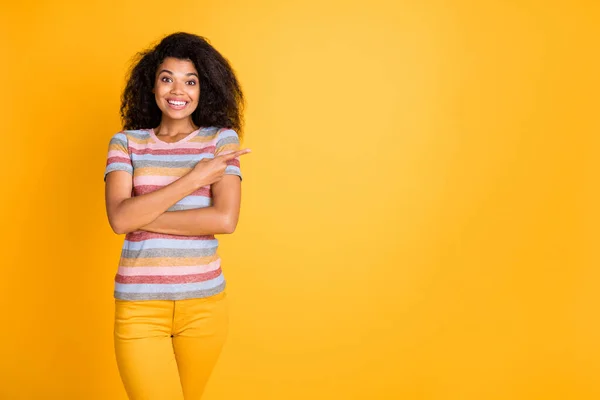 Portrait of her she nice attractive cheerful girlish glad wavy-haired girl wearing striped tshirt pointing forefinger aside ad advert isolated on bright vivid shine vibrant yellow color background — Stock Photo, Image