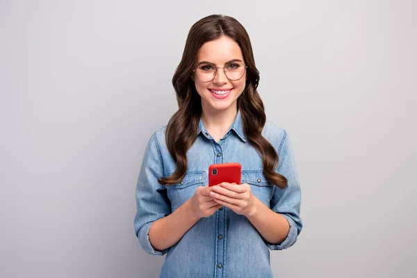 Foto de hermosa freelancer creativa dama sosteniendo la navegación por teléfono escribir post nuevo blog buen humor desgaste especificaciones casual jeans mezclilla aislado gris color fondo — Foto de Stock