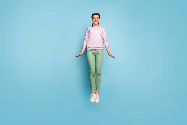 Full body photo of beautiful lady jumping high up enjoy amazing sunny spring day weather rejoicing good mood wear casual pink pullover green pants isolated blue color background — 图库照片