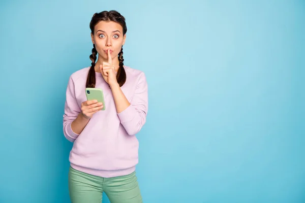 Foto van mooie dame houden telefoon vinger op lippen lezen geheime informatie wilt verbergen voor mensen dragen casual roze trui groene broek geïsoleerde blauwe kleur achtergrond — Stockfoto