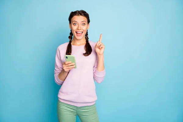 Photo of beautiful lady funny pigtails hold telephone have crazy new blog post advert text idea raise index finger wear casual pink sweater green pants isolated blue color background — ストック写真