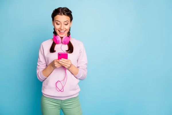 Foto der schönen Dame halten Telefon mit neuen modernen Kopfhörern Anschluss an Smartphone cool Soundqualität tragen lässig rosa Pullover grüne Hosen isoliert blaue Farbe Hintergrund — Stockfoto