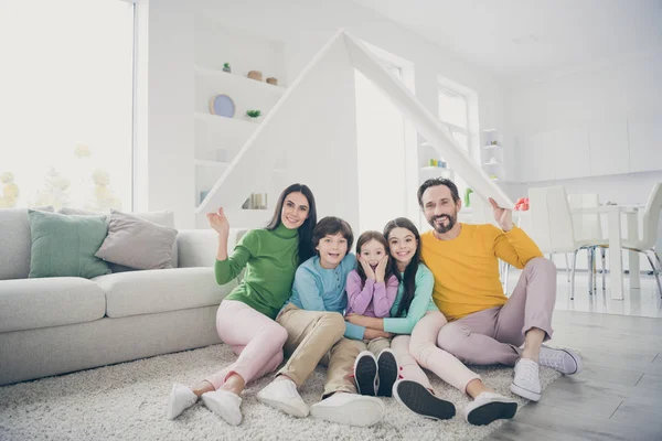 Retrato de agradable atractiva encantadora familia alegre emocionada tres niños pre-adolescentes sentados en el suelo de la alfombra sosteniendo en el lugar del techo de la mano buen cambio en la casa de estilo interior blanco claro sala de estar plana —  Fotos de Stock