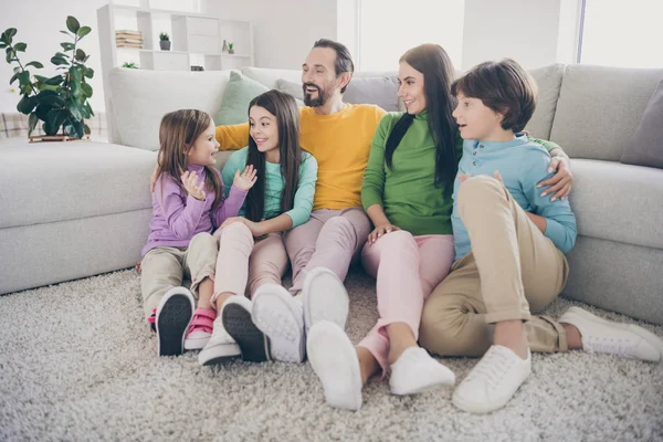 Pouco bonito criança mais jovem sentar tapete chão perto sofá sofá dizer dizer jardim de infância novidade pessoas amando família ouvir divirta-se papai mamãe abraço três crianças pré-adolescentes na sala de casa — Fotografia de Stock