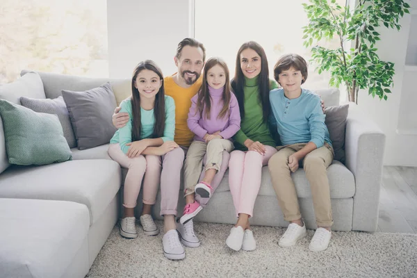 Volledige lengte foto van positieve vrolijke familie drie tieners schooljongen schoolmeisje jongere zus papa mama knuffel omarmen zitten bank chillen in huis woonkamer — Stockfoto