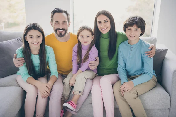 Positiv kärleksfull glad idealisk familj koncept. Mamma pappa sitta soffa kram omfamna hennes tre barn skolpojke skolflicka i huset vardagsrum — Stockfoto