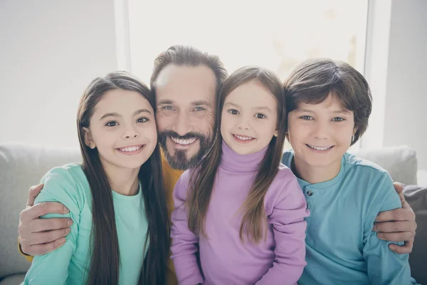 Портрет позитивної веселої люблячої сім'ї тато обіймає своїх милих дітей двоє дівчаток хлопчик син молодша сестра сидить у будинку в приміщенні — стокове фото