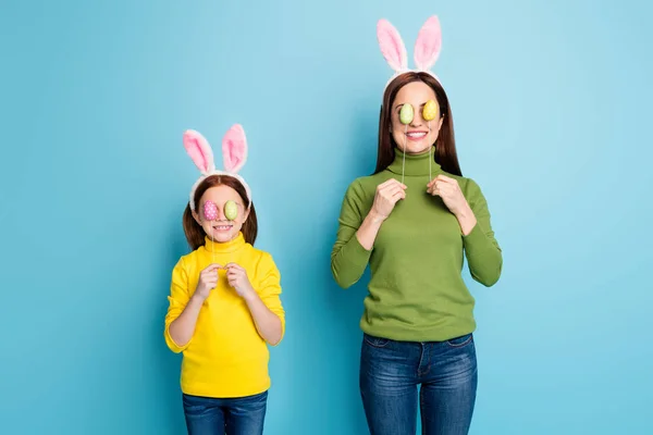 Portrait of nice attractive lovely childish playful cheerful cheery girls covering eyes with eggs sticks having fun isolated over bright vivid shine vibrant blue color background — Stock Photo, Image