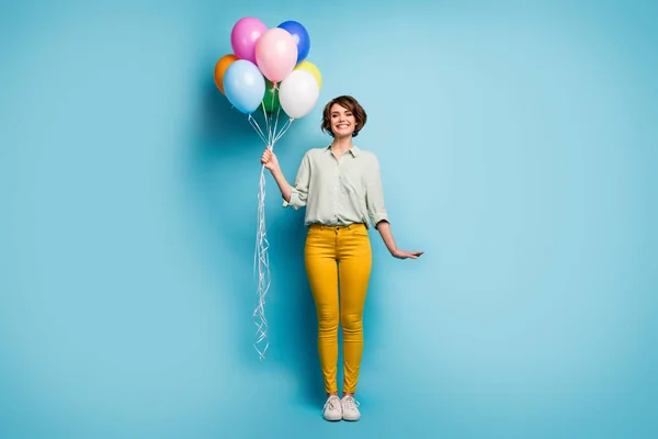 Foto de longitud completa de bastante lindo adorable dama fiesta de cumpleaños sorpresa celebrar muchos globos de aire coloridos desgaste casual camisa verde pantalones amarillos zapatos aislados de color azul de fondo — Foto de Stock