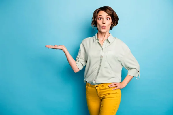 Φωτογραφία από αρκετά αστείο κυρία κατέχουν ανοιχτό χέρι κενό χώρο καινοτομία πώληση προϊόν απίστευτη χαμηλή τιμή φορούν casual πράσινο πουκάμισο κίτρινο παντελόνι απομονωμένο μπλε φόντο χρώμα — Φωτογραφία Αρχείου