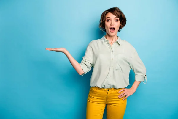 Foto de señora bastante divertida mantenga el brazo abierto espacio vacío novedad venta producto increíble precio bajo desgaste casual camisa verde pantalones amarillos aislados color azul fondo —  Fotos de Stock