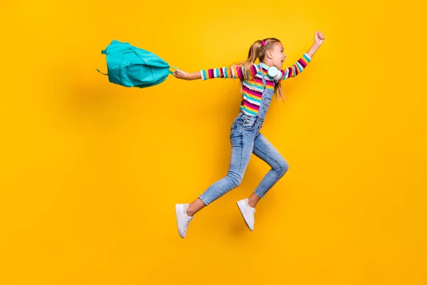 Sí, empiezan las vacaciones. Perfil de tamaño completo lado loco colegial salto correr celebrar mochila azul bolsa tienen auriculares desgaste a rayas suéter vaqueros aislados sobre brillante brillo amarillo color fondo —  Fotos de Stock