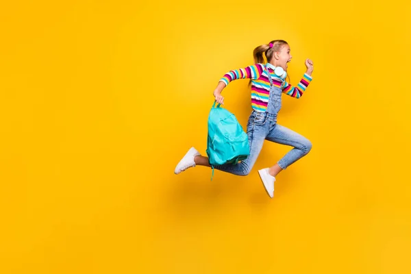 Full body profil boczny zdjęcie szalone schoolchild skok uruchomić szkoły rabaty trzymać niebieski plecak torba nosić paski sweter dżinsy szelki kombinezony odizolowane jasny połysk żółty kolor tło — Zdjęcie stockowe