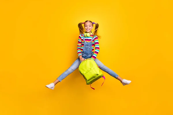 Full size foto vrolijke schoolkind springen dragen headset gestreepte trui jeans spijkerbroek tas rugzak genieten lagere school les geïsoleerd over helder glans gele kleur achtergrond — Stockfoto