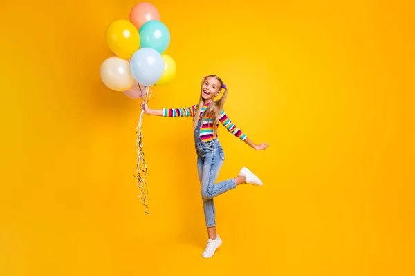 Full size photo of positive cheerful energetic children hold many baloons enjoy rest relax event occasion wear style stylish trendy outfit gumshoes isolated over yellow color background — 스톡 사진