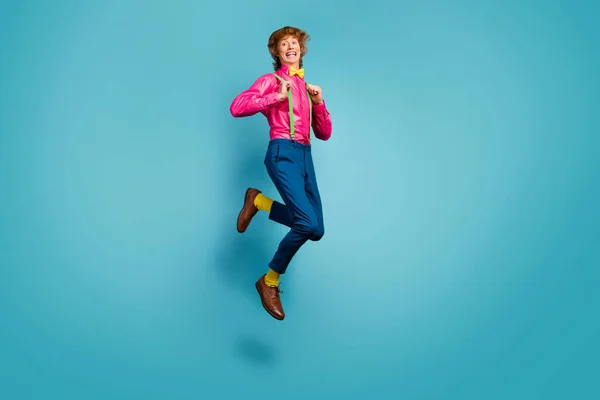 Full length photo of enthusiastic cheerful guy jump enjoy spring free time holiday jump pull suspenders wear trendy pink shoes isolated over blue color background — Stock Photo, Image