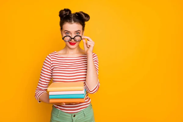 Foto av student nörd dam hålla många böcker ser knepigt att ta av roliga missfoster glasögon bära randig röd vit skjorta gröna byxor isolerad ljus gul färg bakgrund — Stockfoto