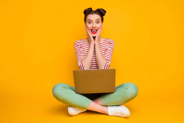 Foto de tamaño completo de la señora bastante impactada sentarse piernas cruzadas sostener portátil leer buena información ropa de Internet rayas rojo blanco camisa verde pantalones zapatos aislados de color amarillo fondo — Foto de Stock